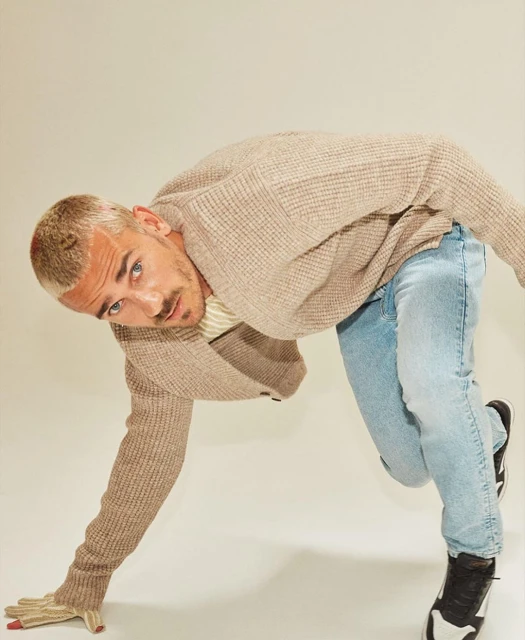 Indoor shot of a blonde adult male in a beige cardigan and light blue jeans, leaning forward with one hand on the floor.