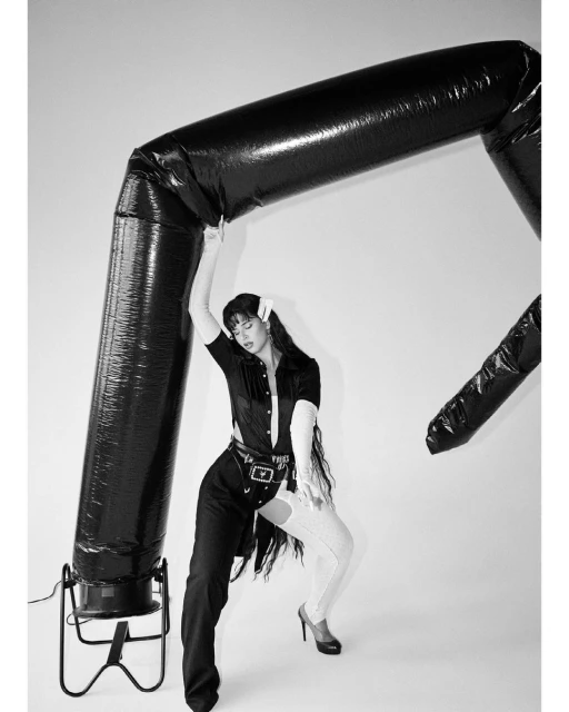 Adult female posing with an inflatable tube in a monochrome studio shot, wearing a collared shirt and mismatched pants.