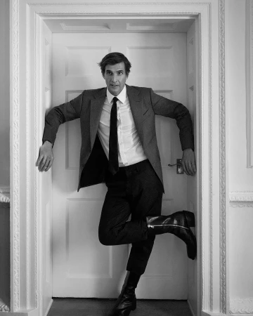 Monochrome portrait of a man in a suit jacket, white shirt, and boots posed inside a paneled doorway in Paris.