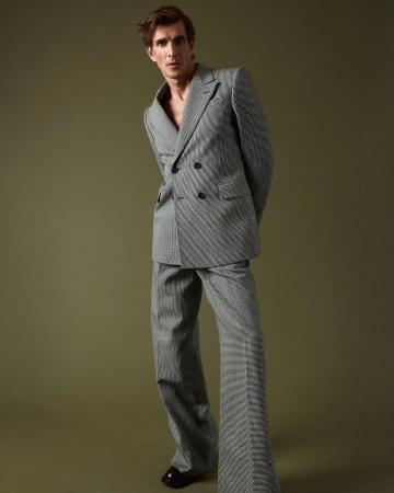 Man in a grey patterned double breasted suit posing against a solid olive green studio backdrop by Daniel Riera