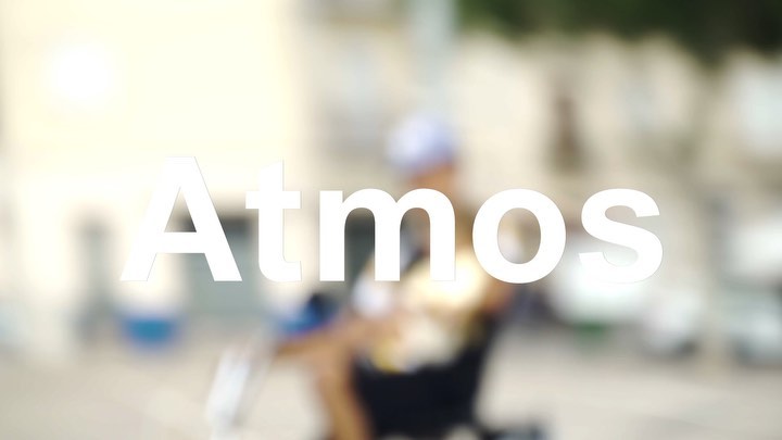 Blurred view of a person in a wheelchair with Atmos text overlay. The image has a soft focus, creating a hazy, dreamlike effect.