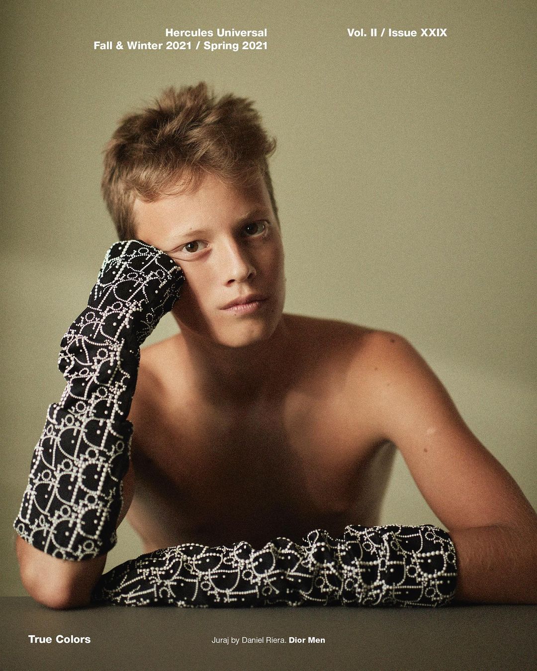 Fashion editorial shot of a shirtless young man in patterned gloves, against a neutral background. Magazine cover with text.