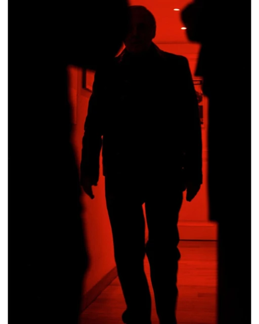 Silhouette of an adult male in a suit walking through a hallway with a red glow, creating a sense of mystery and anonymity.