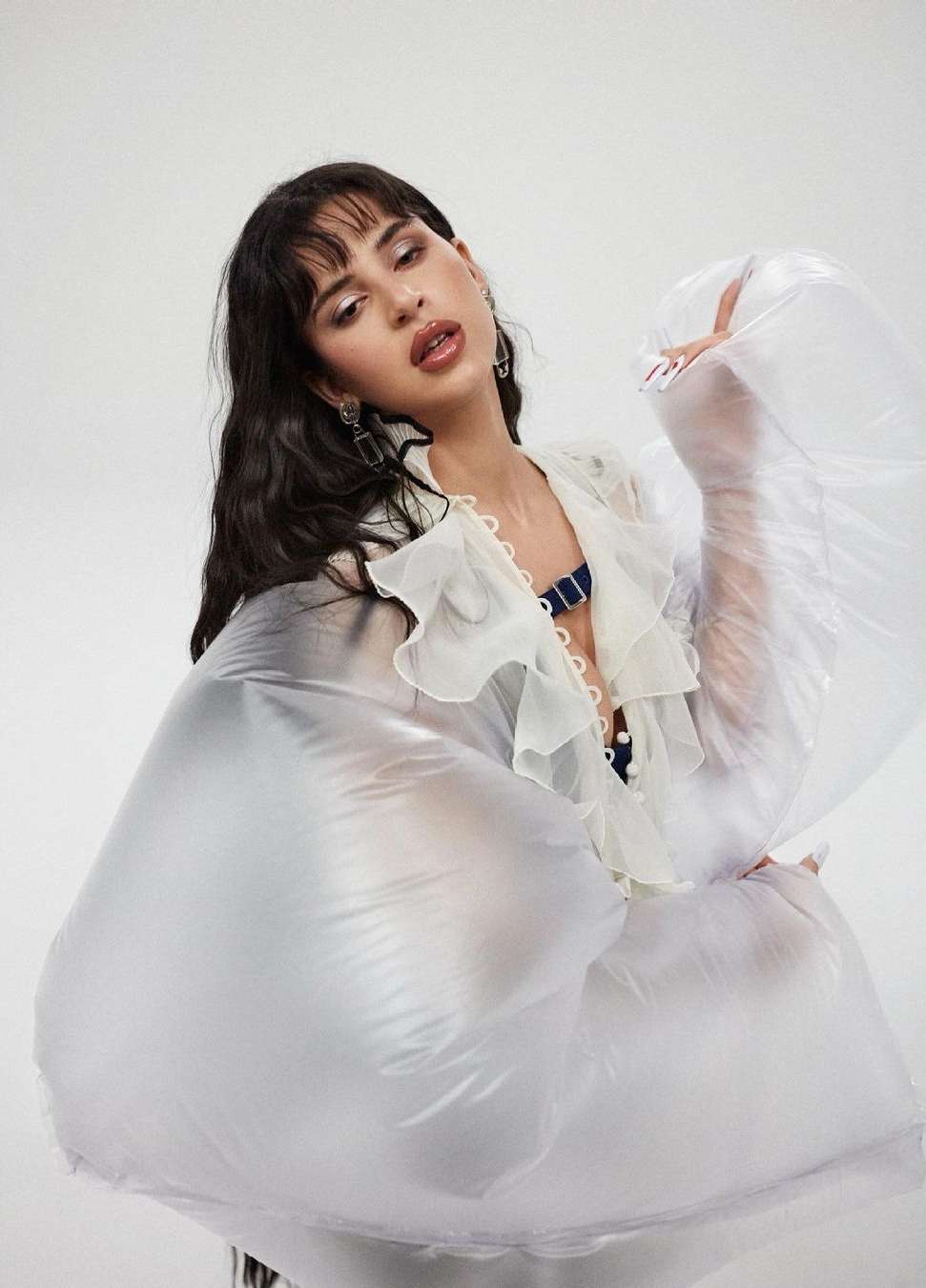 Portrait of a young woman in a ruffled blouse and puffed transparent sleeves against a white background, looking up.