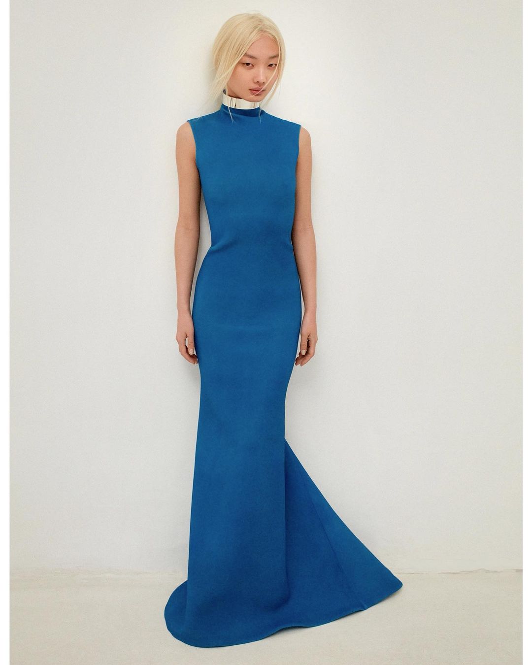 An Asian woman poses in a formal blue dress against a white background, creating a classic, elegant fashion portrait.