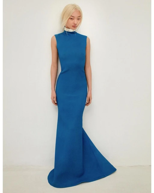 An Asian woman poses in a formal blue dress against a white background, creating a classic, elegant fashion portrait.