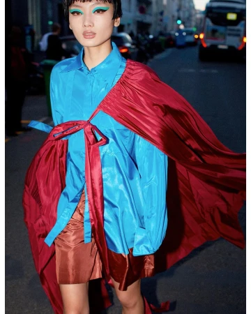 Model in vivid blue shirt and red satin cape on a Paris street captured by Daniel Riera