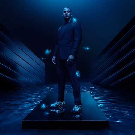 Stylish adult man in a dark suit stands on a platform in a blue-lit studio with artistic butterfly effects in a fashion photography shot.