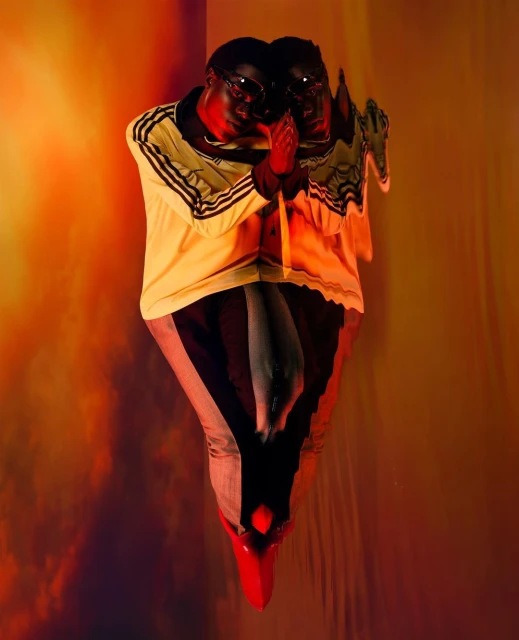Fashion editorial featuring two dark-skinned adult males wearing sunglasses and retro-style sports jackets in a studio with orange lighting.