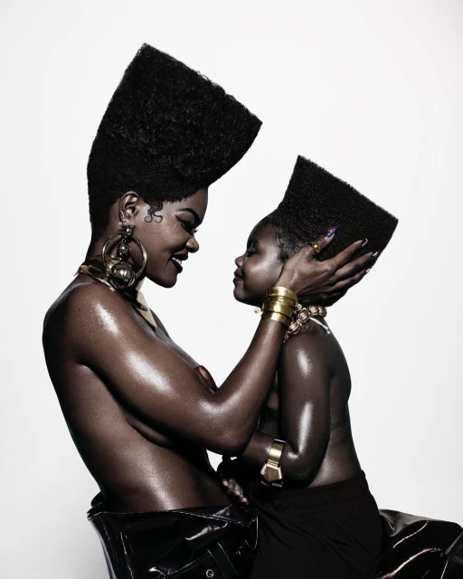 A striking image captures an adult and a child with tall afro hairstyles, adorned in gold jewelry, set against a clean white backdrop.