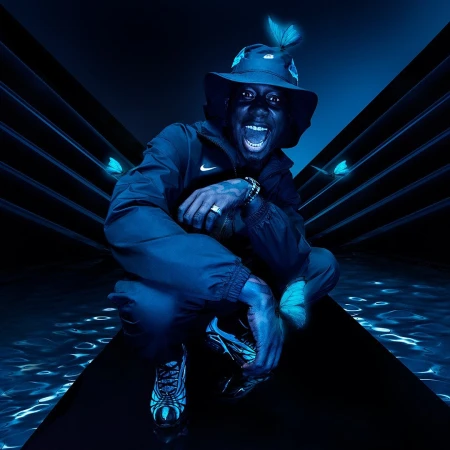 A dark-skinned man with a bucket hat and jacket, crouched indoors with butterflies and digital water effects, bathed in blue light.