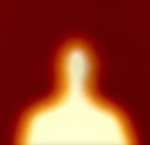 Abstract blurred silhouette of a person against a red background, creating an indistinct figure with a glowing orange aura.