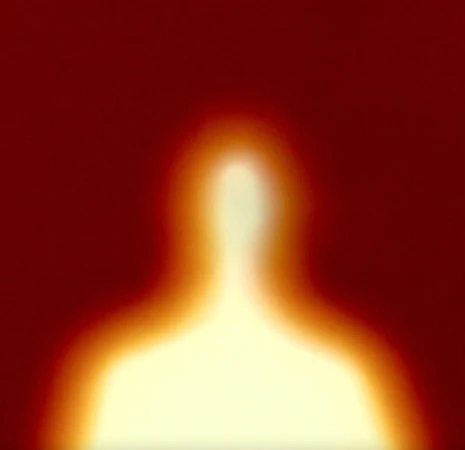 Abstract blurred silhouette of a person against a red background, creating an indistinct figure with a glowing orange aura.
