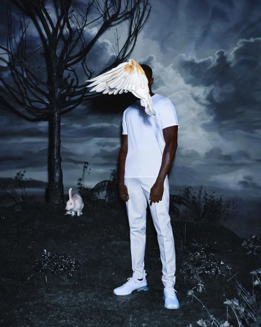 Artistic portrait of an adult male standing in a field with a white rabbit in the background, face partially covered by a bird wing.