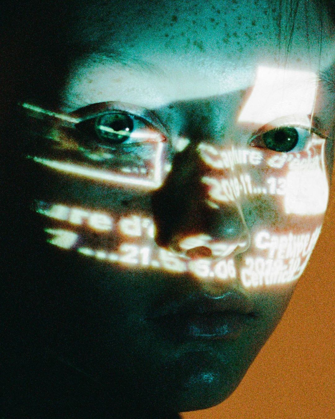 Woman's face close-up with projected digital text. Cyan and orange color palette with an artistic and technological feel. 