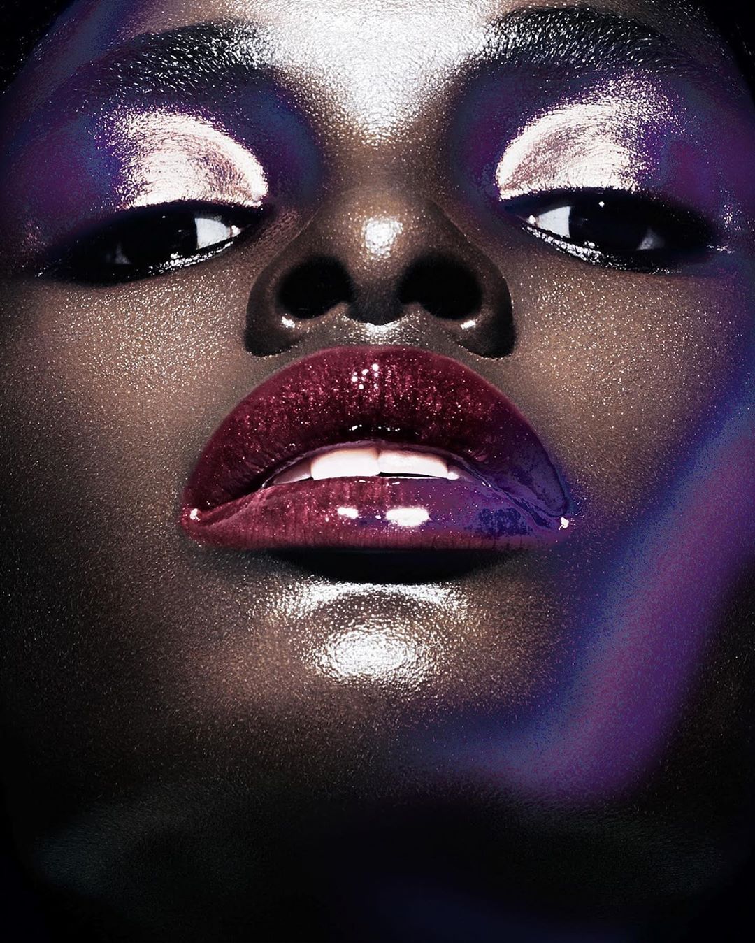 Close-up shot of an African American woman's face, showcasing glossy lips, shimmery eyeshadow, and flawless skin with soft, dramatic lighting.
