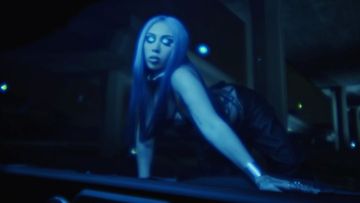 Adult female with blue hair and pale complexion on hands and knees, wearing dark clothing in dim interior environment.