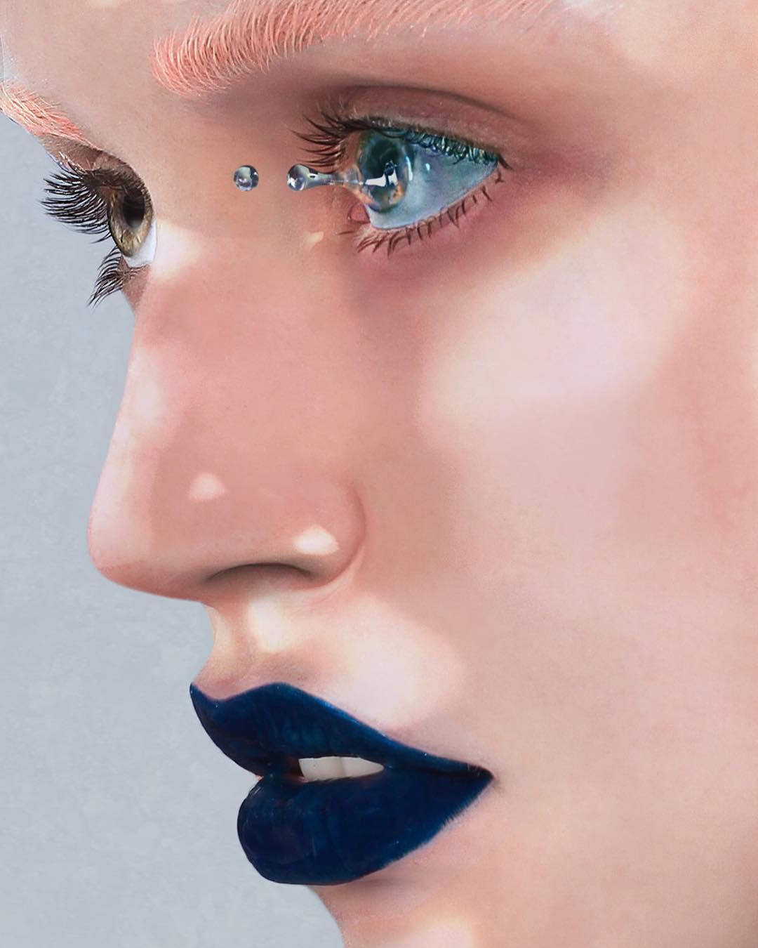 Close-up of a woman's face featuring light skin, blue lips, and a cosmetic teardrop design around the eye in a surreal beauty portrait.