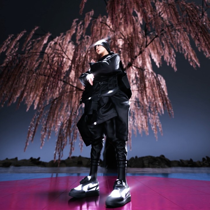 Person in black outfit with white-striped shoes poses in front of a digital backdrop of dark trees and a lake under a night sky.