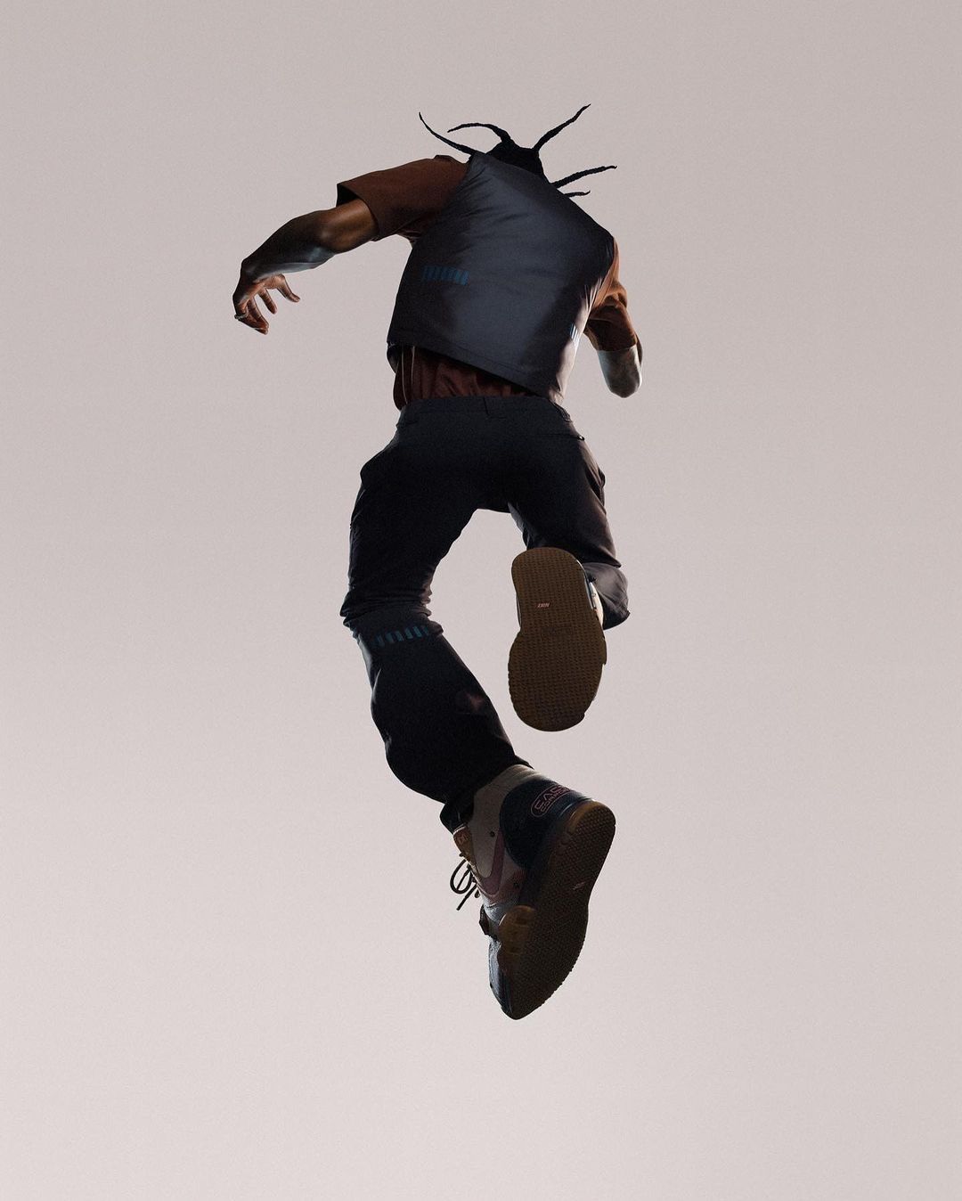 Full shot of a man in streetwear jumping mid-air, with a neutral background showcasing his casual yet stylish urban outfit.