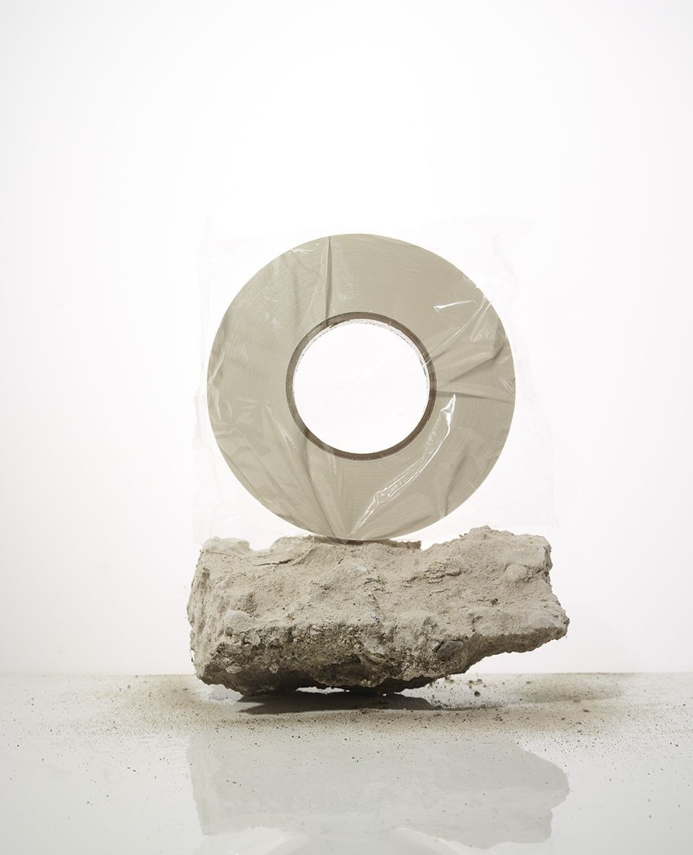 Roll of grey tape resting on a piece of light grey rock against a bright white background in a studio setting with neutral lighting.