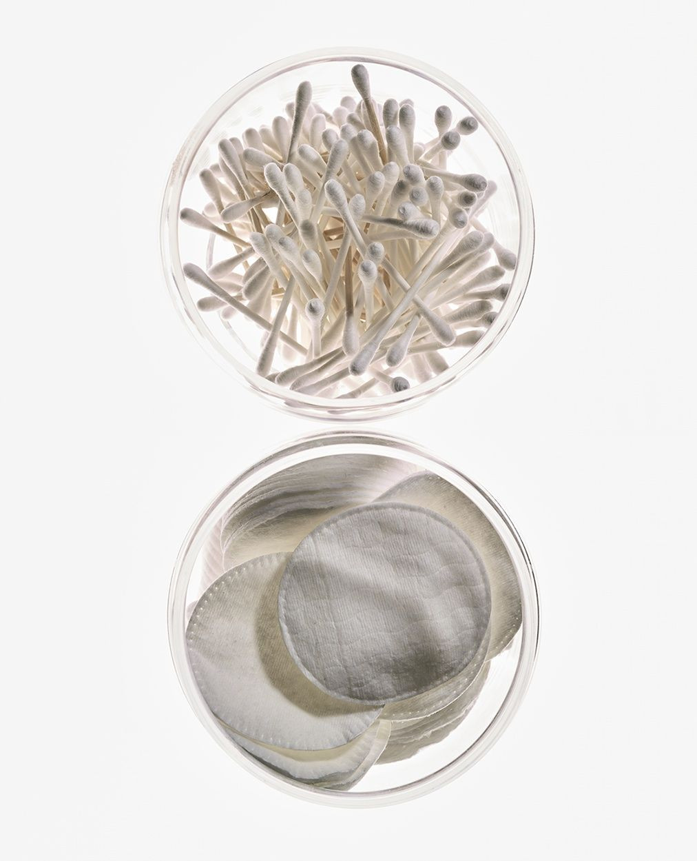 Overhead shot: Cotton swabs and cotton pads arranged in clear jars against a bright white backdrop, ideal for beauty or healthcare themes.