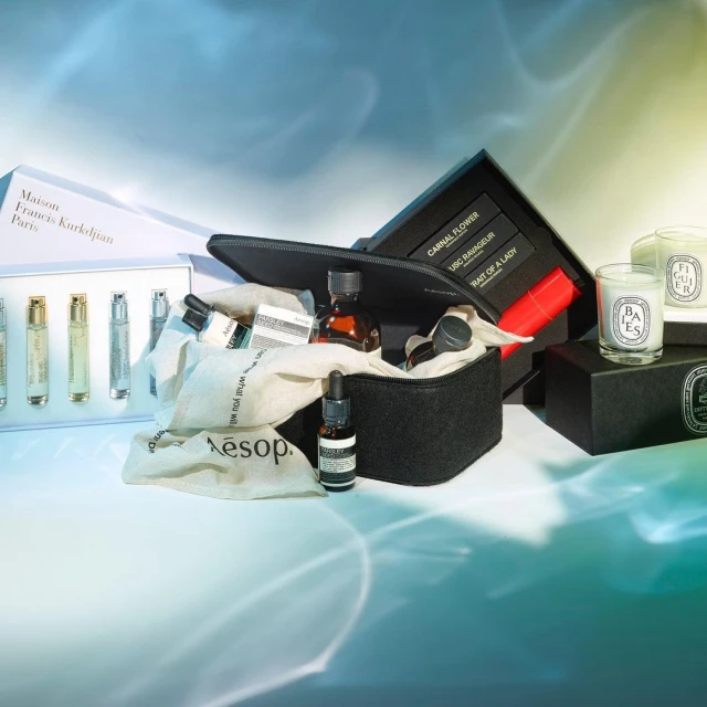 Cosmetic product arrangement featuring Aesop skincare, fragrance samples, candles, and makeup in a stylish black cosmetic bag.