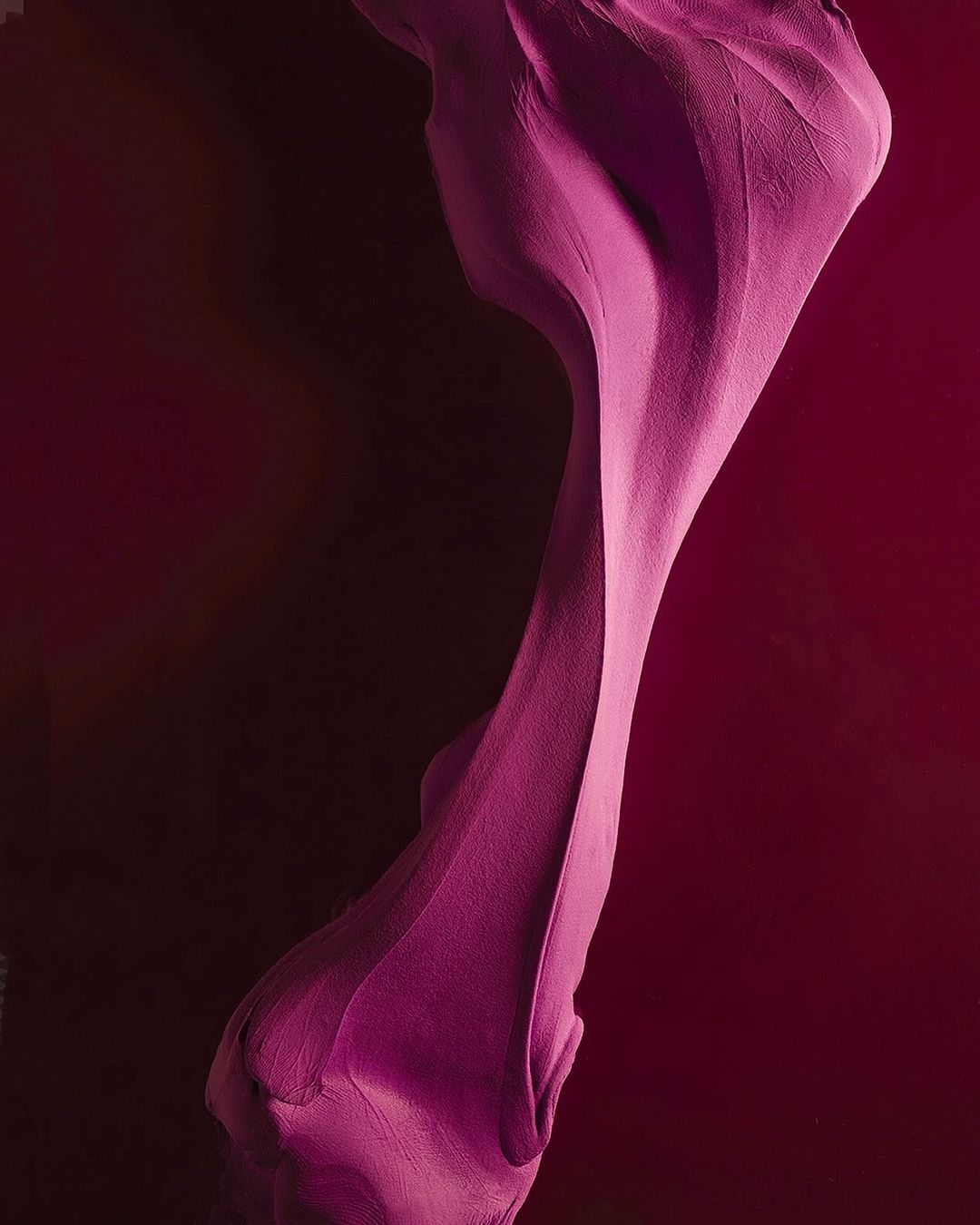 Abstract magenta fabric undulates against a dark red background, creating a visually striking and textured artistic display.