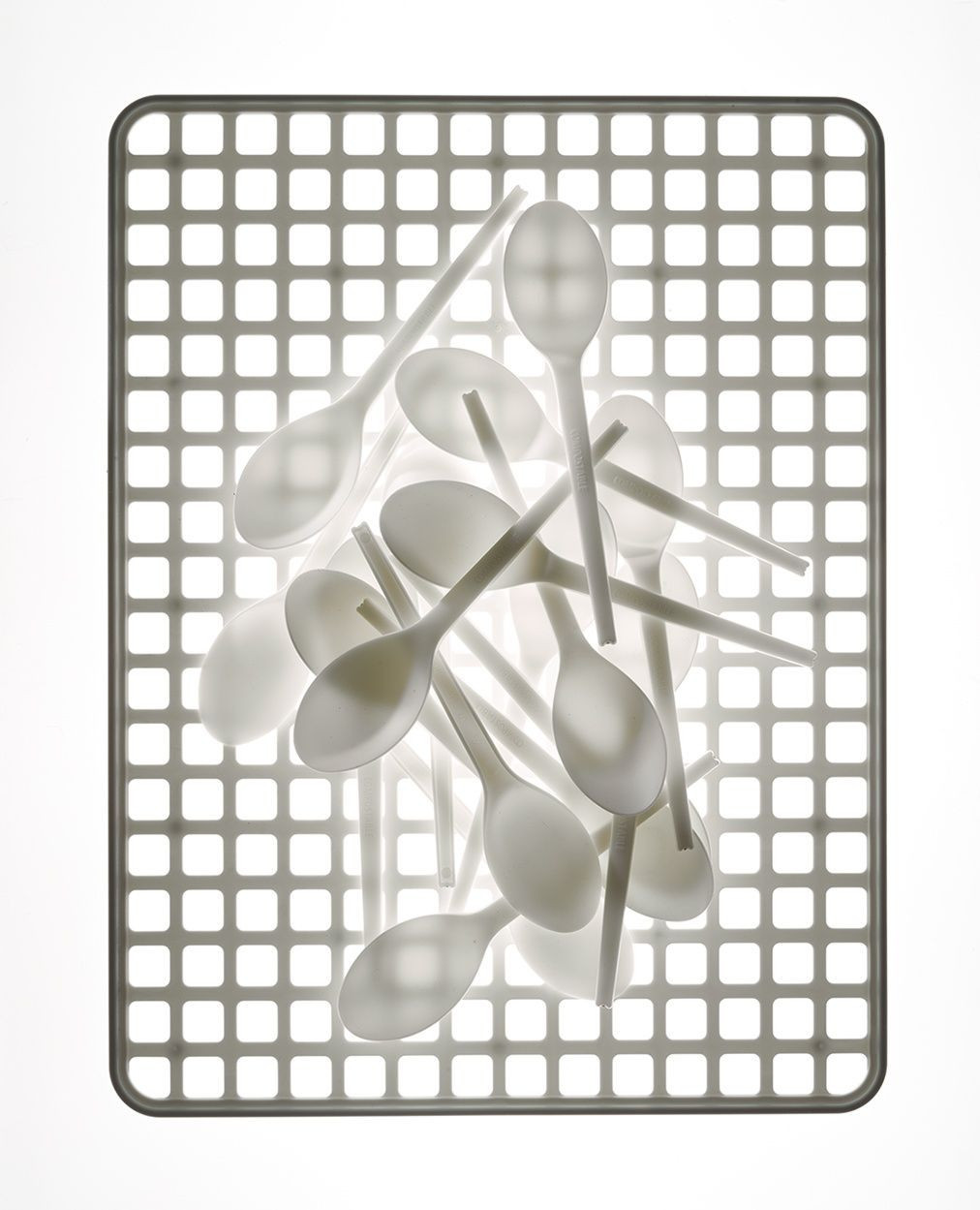 Pile of white plastic spoons arranged on a gray grid surface under bright, even lighting, creating a clean, minimalist food service image.