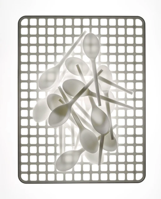 Pile of white plastic spoons arranged on a gray grid surface under bright, even lighting, creating a clean, minimalist food service image.