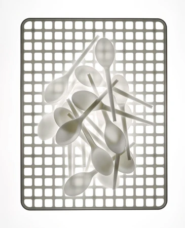 Pile of white plastic spoons arranged on a gray grid surface under bright, even lighting, creating a clean, minimalist food service image.