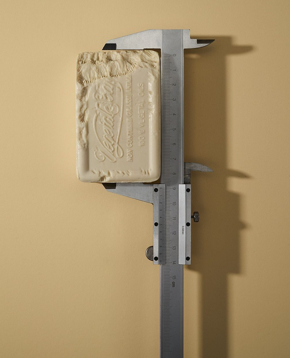 Close-up of a bar of Vegetale soap being measured with a silver-colored caliper against a plain beige background in studio lighting.