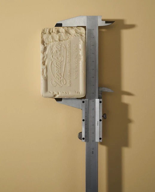 Close-up of a bar of Vegetale soap being measured with a silver-colored caliper against a plain beige background in studio lighting.