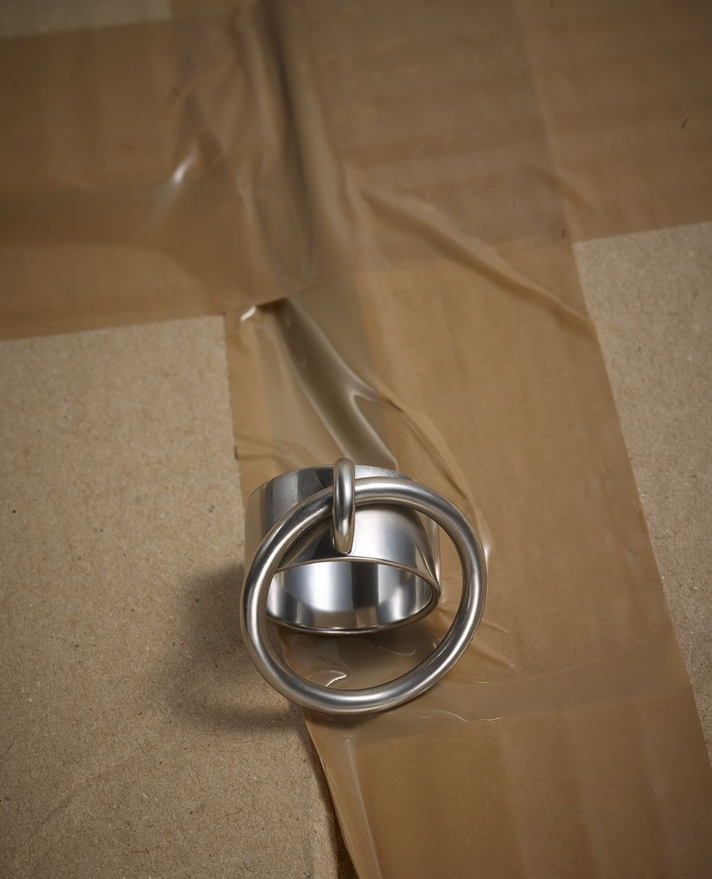 Close-up of a shiny metal ring attached to a metal cylinder, resting on a surface covered with brown masking tape.