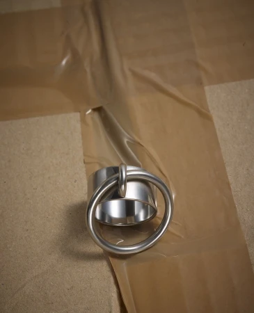 Close-up of a shiny metal ring attached to a metal cylinder, resting on a surface covered with brown masking tape.