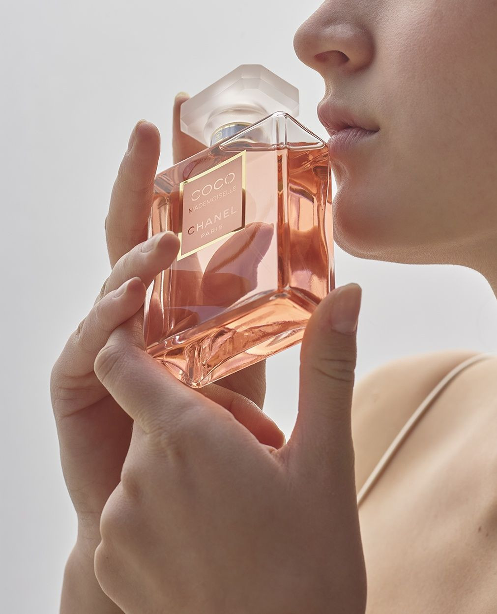 Woman holds a bottle of Chanel Coco Mademoiselle perfume, smelling the fragrance against a clean white background in a beauty shot.