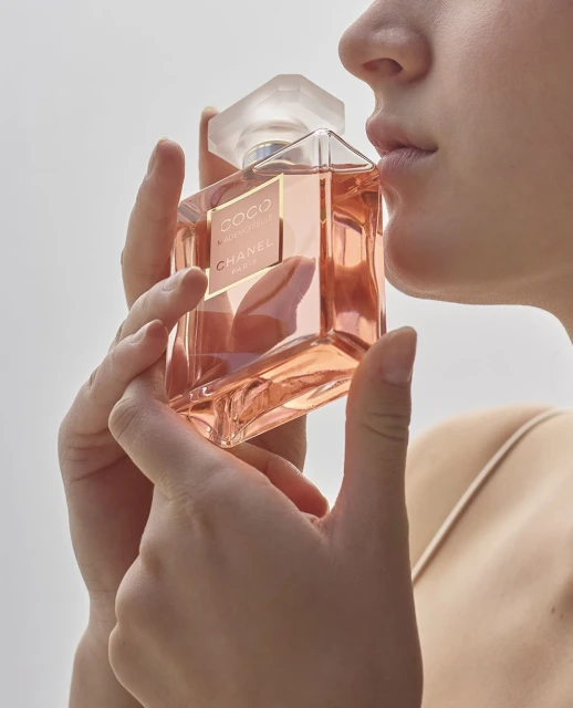Woman holds a bottle of Chanel Coco Mademoiselle perfume, smelling the fragrance against a clean white background in a beauty shot.