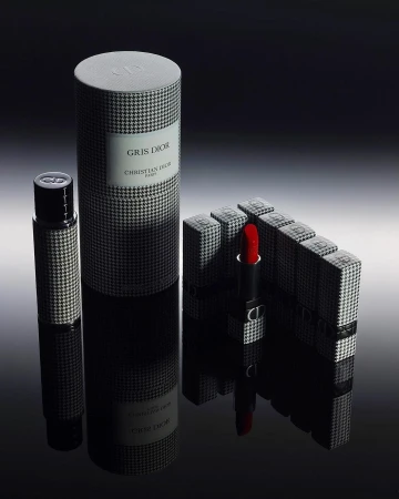 Close-up studio shot of Dior makeup and fragrances. The products feature black and white houndstooth patterns and reflect on a shiny surface.