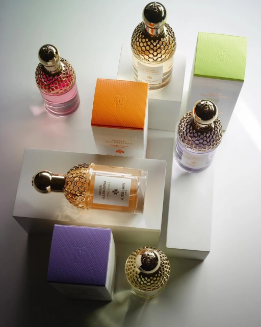 Several colorful glass perfume bottles with gold caps arranged on white geometric blocks against a soft studio background, product photography.