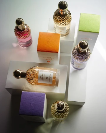 Several colorful glass perfume bottles with gold caps arranged on white geometric blocks against a soft studio background, product photography.