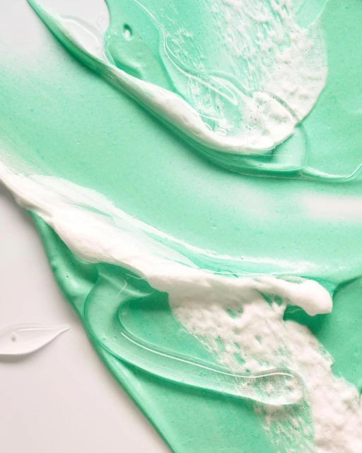 Textured shot of light turquoise and white cream, swirled and layered, creating a visually appealing and textured abstract pattern.