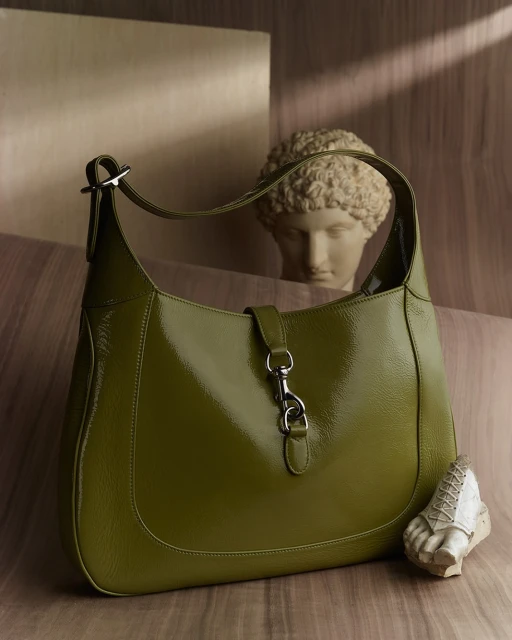 Olive-green leather hobo bag with a silver clasp. The purse is positioned next to a partially visible sculpture bust and foot.