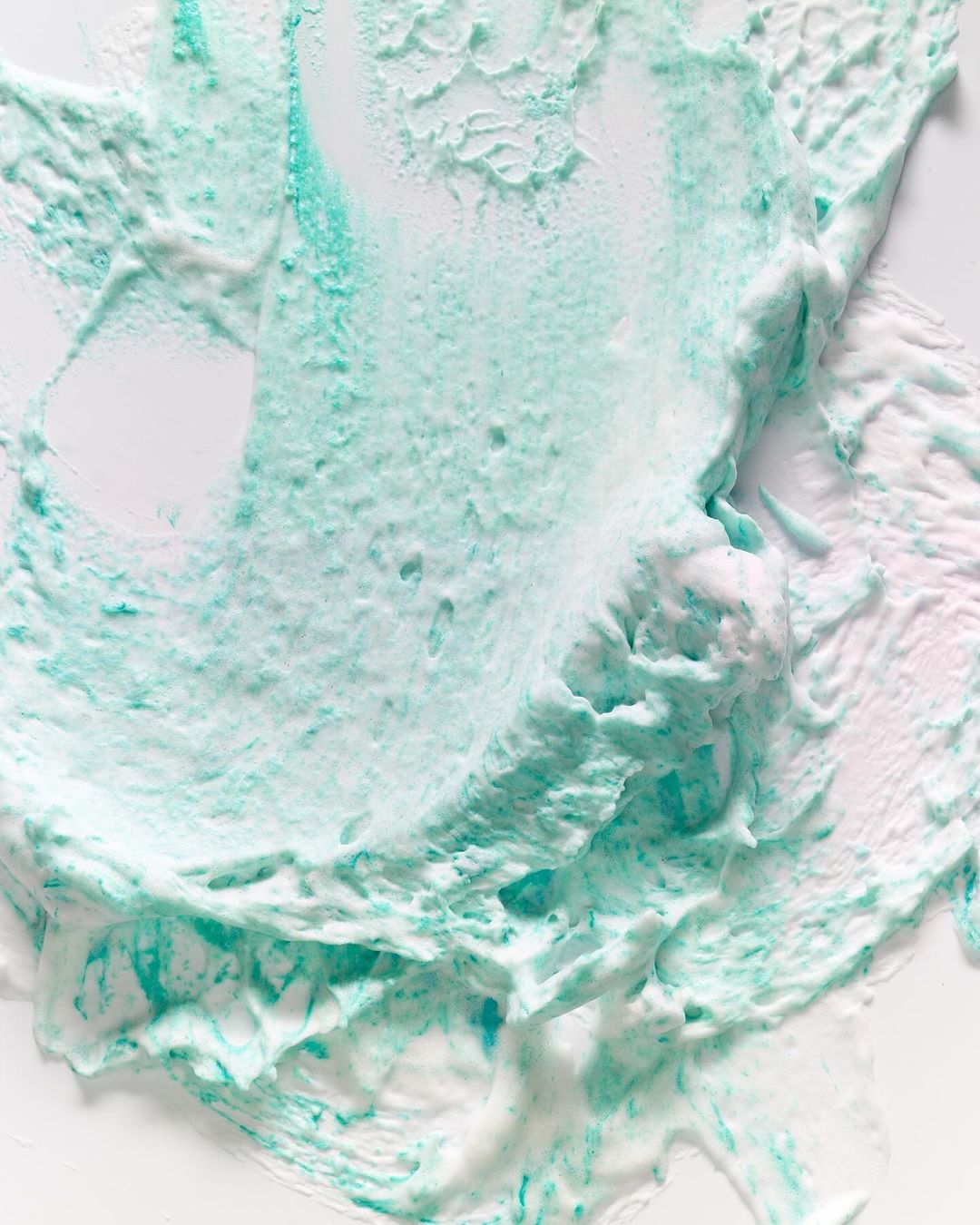 Close-up of a smear of teal and white cosmetic cream. The texture is thick and swirled, resembling an abstract artistic creation.