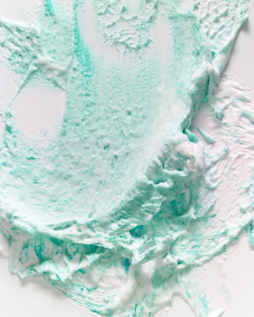 Close-up of a smear of teal and white cosmetic cream. The texture is thick and swirled, resembling an abstract artistic creation.