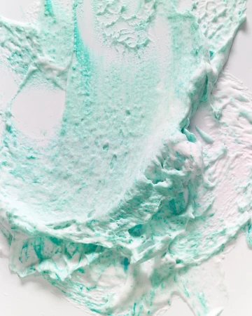 Close-up of a smear of teal and white cosmetic cream. The texture is thick and swirled, resembling an abstract artistic creation.