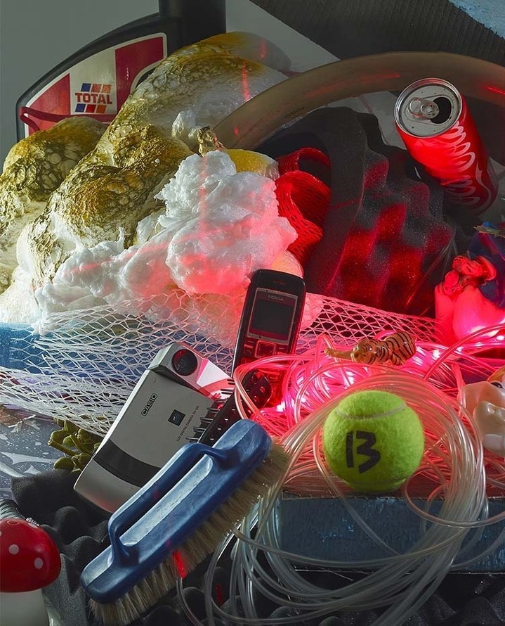 Still life featuring motor oil, tennis ball, soda can, cell phone, and cleaning brush arranged in a studio setting with red accent lighting.