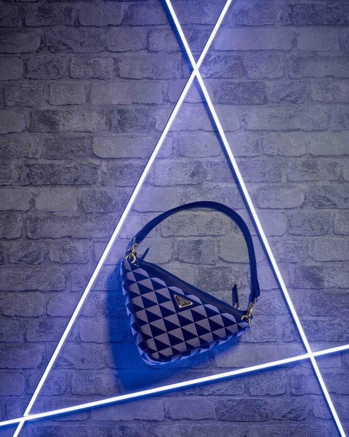 Prada Cleo handbag with a geometric pattern on a grey brick wall with neon triangle lighting for a fashion or product shot.