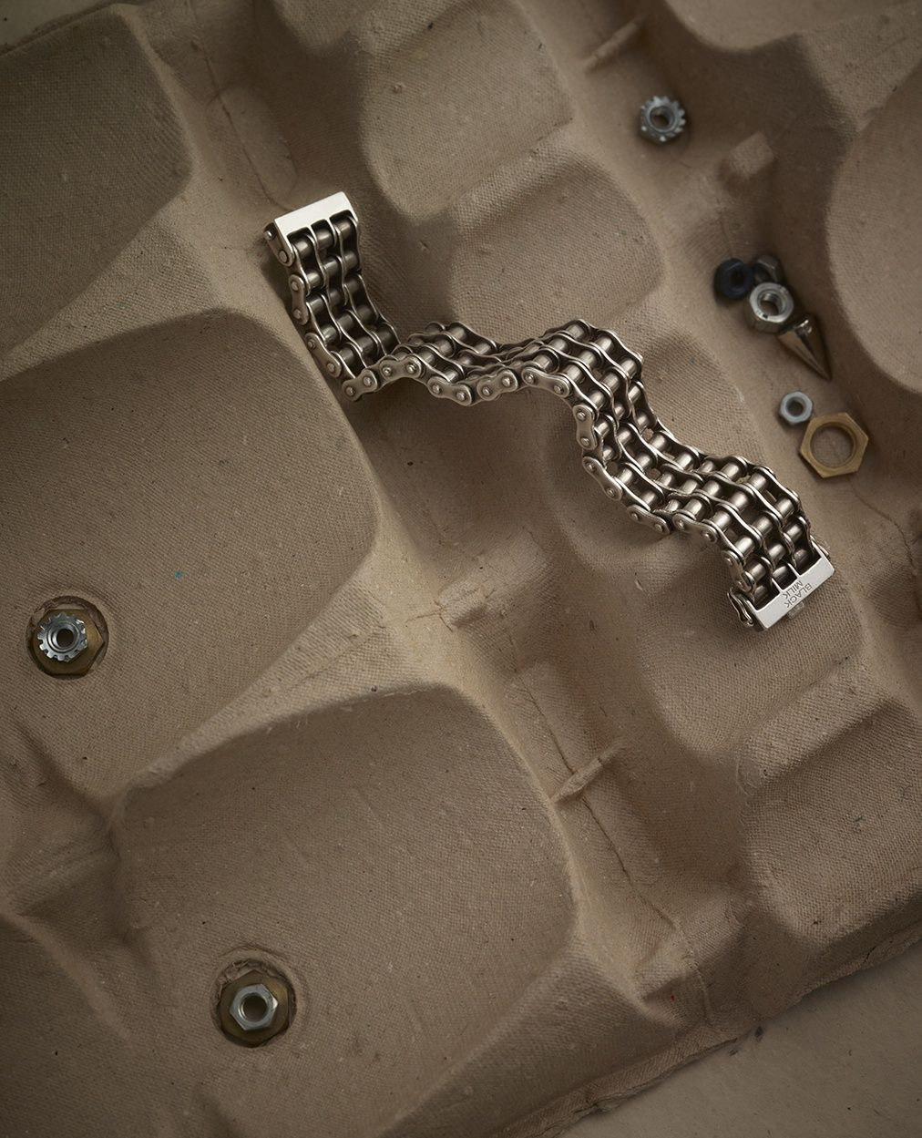 Silver chain bracelet on an egg carton, with nuts and bolts scattered around, product shot with neutral background.