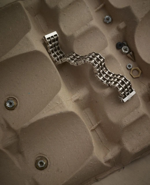 Silver chain bracelet on an egg carton, with nuts and bolts scattered around, product shot with neutral background.