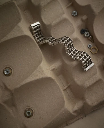 Silver chain bracelet on an egg carton, with nuts and bolts scattered around, product shot with neutral background.